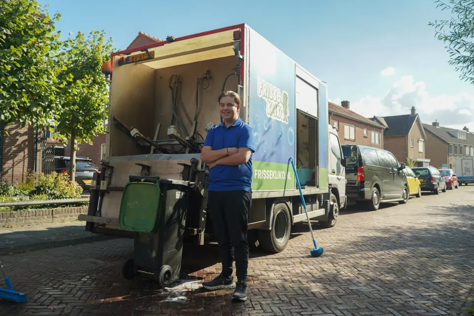 Medewerker van Frisse Kliko naast de reinigingswagen in een woonstraat.